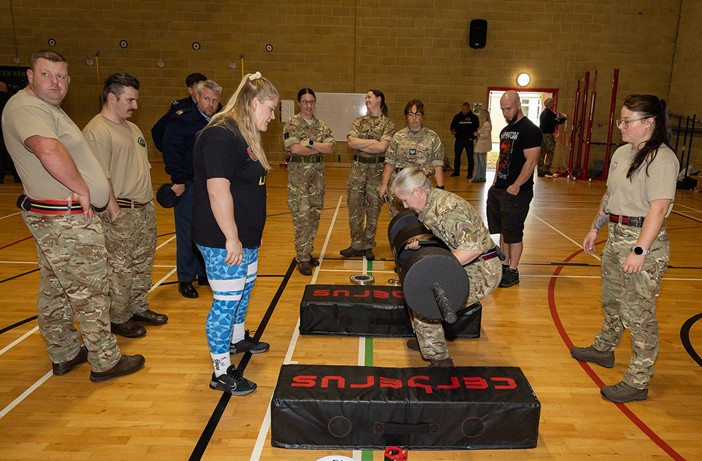 Military personnel watch a demonstration of a weight lifting challenge.